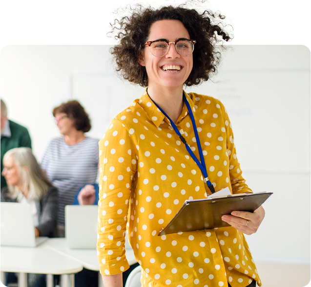 Educadora sorrindo com prancheta em ambiente escolar, representando o apoio pedagógico das escolas parceiras com a Amplia Plataforma de Ensino.