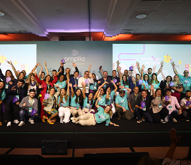 Equipe de educadores celebrando no palco do Conexão Amplia 2025, evento promovido pela Amplia Plataforma de Ensino.